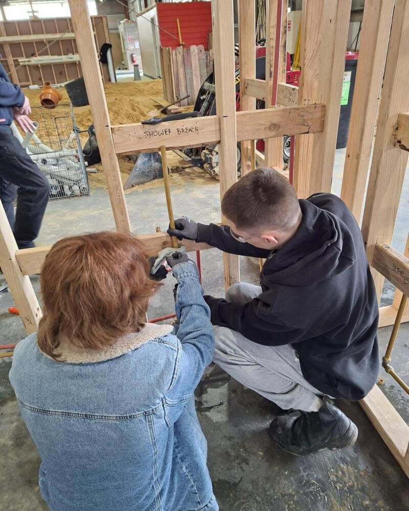 Students helping each other with wooden frame for shower at Swinburne