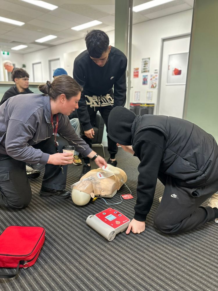 2 students and instructor demonstration a defibrilator on first aid dummy