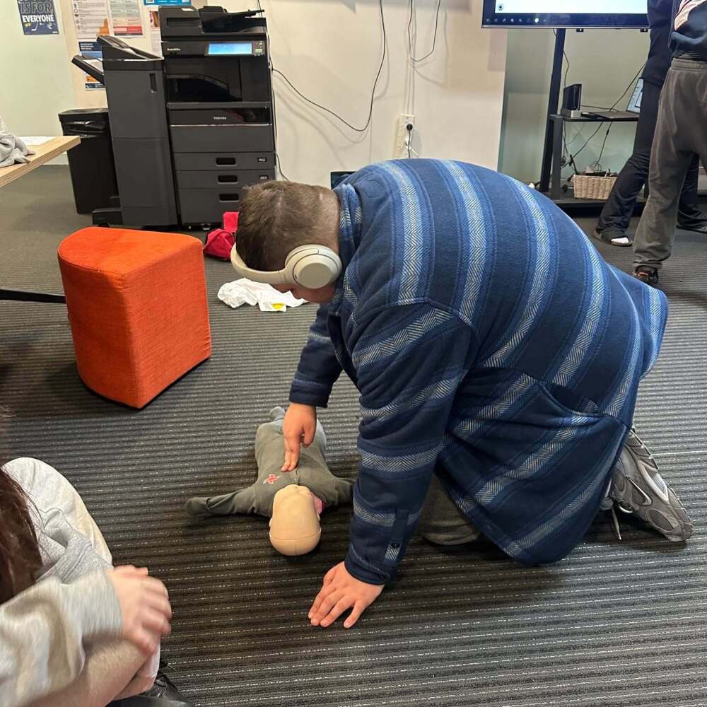 male student in headphones practising chest compressions on dummy of a baby