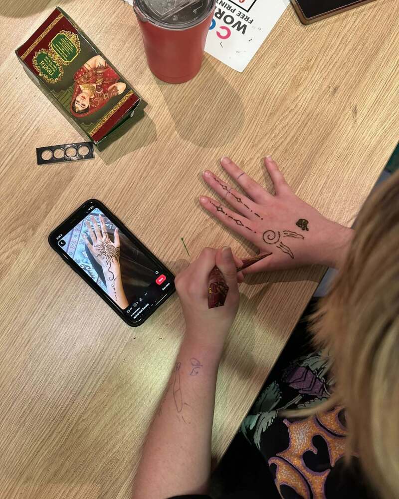 student using her phone to show example of henna design and replicating on her own hand