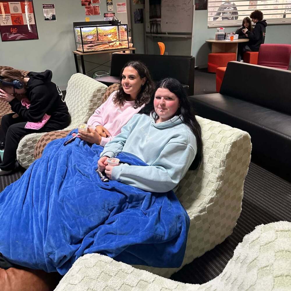 2 female students cosying up on the counch to watch a film