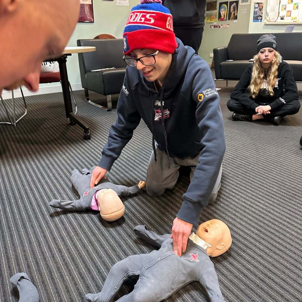 male student in a beanie practising chest compressions on dummy of a baby