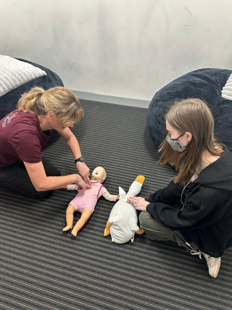 instructor demonstrating to student how to perform CPR on baby dummy 